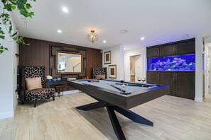 Ein Billardtisch mit modernem Design, ein großer Spiegel und ein Aquarium im Raum.