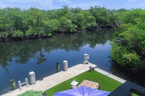A dock with a concrete platform, a grassy area, and a body of water surrounded by dense greenery. - Boater’s Paradise – 60’ Slip & No Fixed Bridges (Boca Raton)