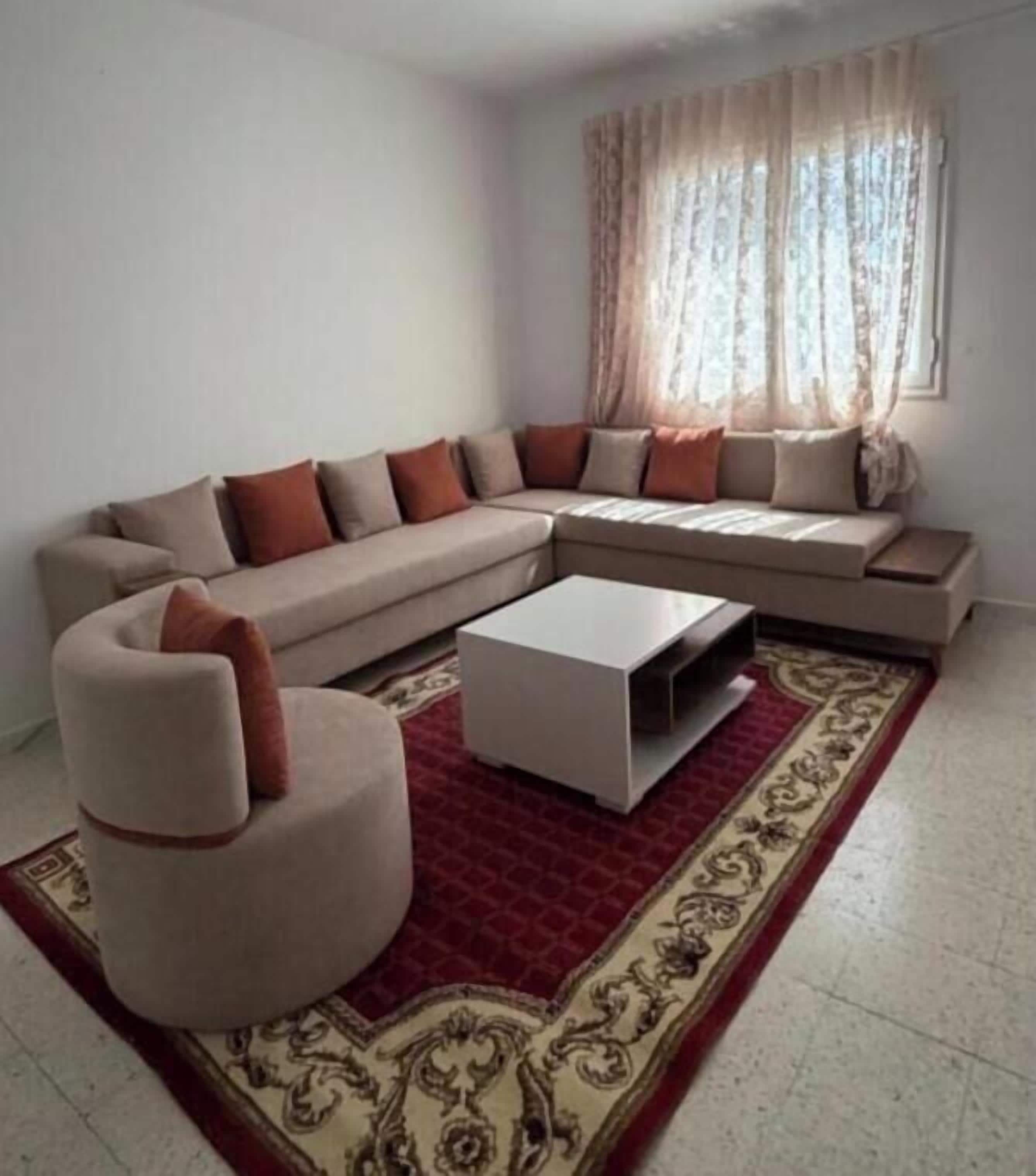 A living room with a beige sectional sofa, a white coffee table, and a red patterned rug.