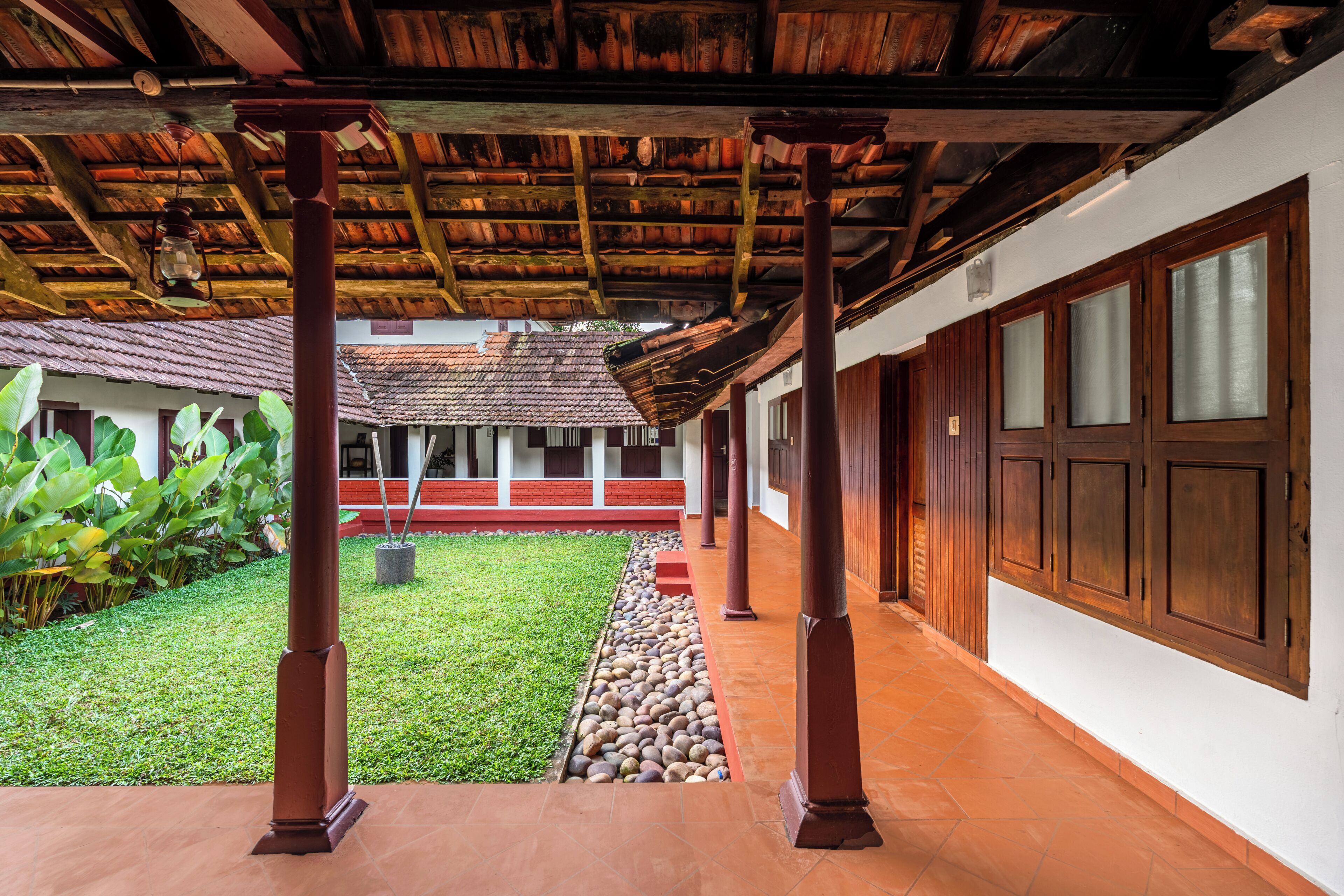 A covered courtyard with a tiled floor, a grassy area, and a row of wooden pillars.