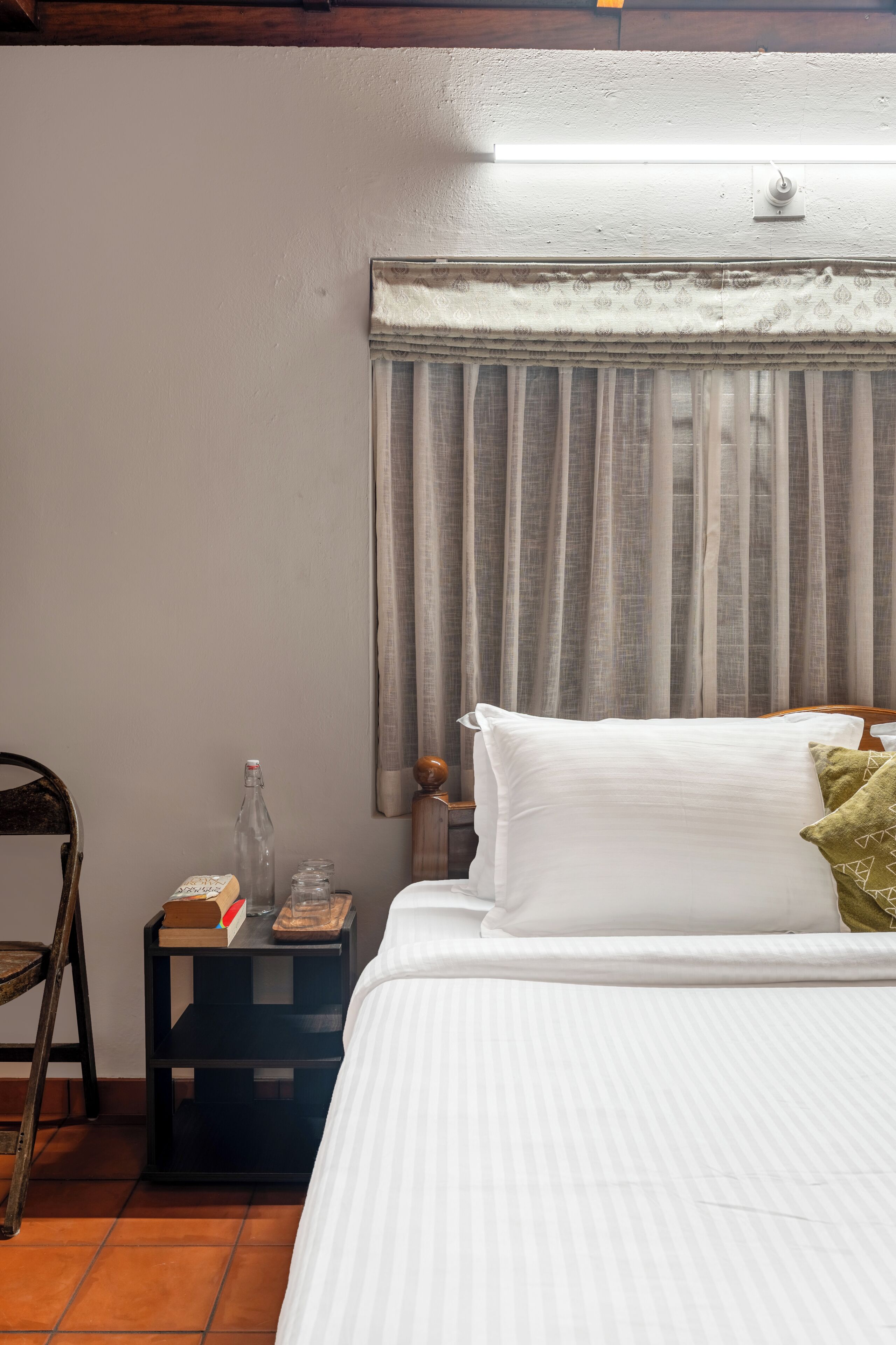 Un dormitorio con cama, mesita de noche, una botella y una silla.