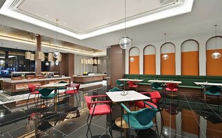 Un restaurante moderno con zona de bar, diversas opciones de asientos, incluyendo cabinas y mesas, y un techo decorativo con iluminación colgante.