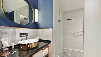Un baño moderno con un lavabo redondo, un espejo grande y una zona de ducha.
