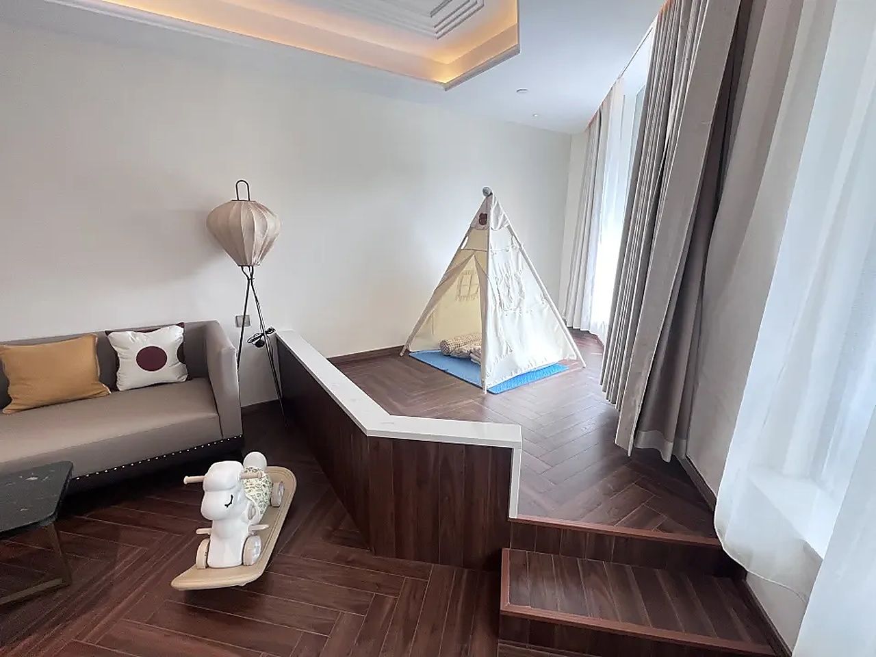 Una sala de estar moderna con un sofá, un pequeño espacio de juego con una carpa y una escalera de madera.