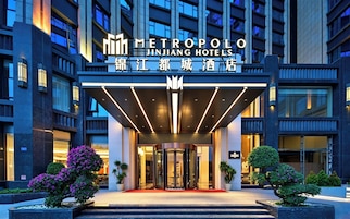 Una entrada moderna a un hotel, con un vestíbulo techado, puertas de vidrio y una alfombra roja que conduce a la entrada.