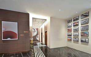 Pasillo de hotel con diseño moderno, que presenta suelo de mármol, pared con fotografías enmarcadas y un motivo de techo distintivo.