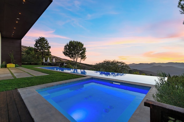 A modern outdoor swimming pool with a clear view of the surrounding landscape and distant mountains.