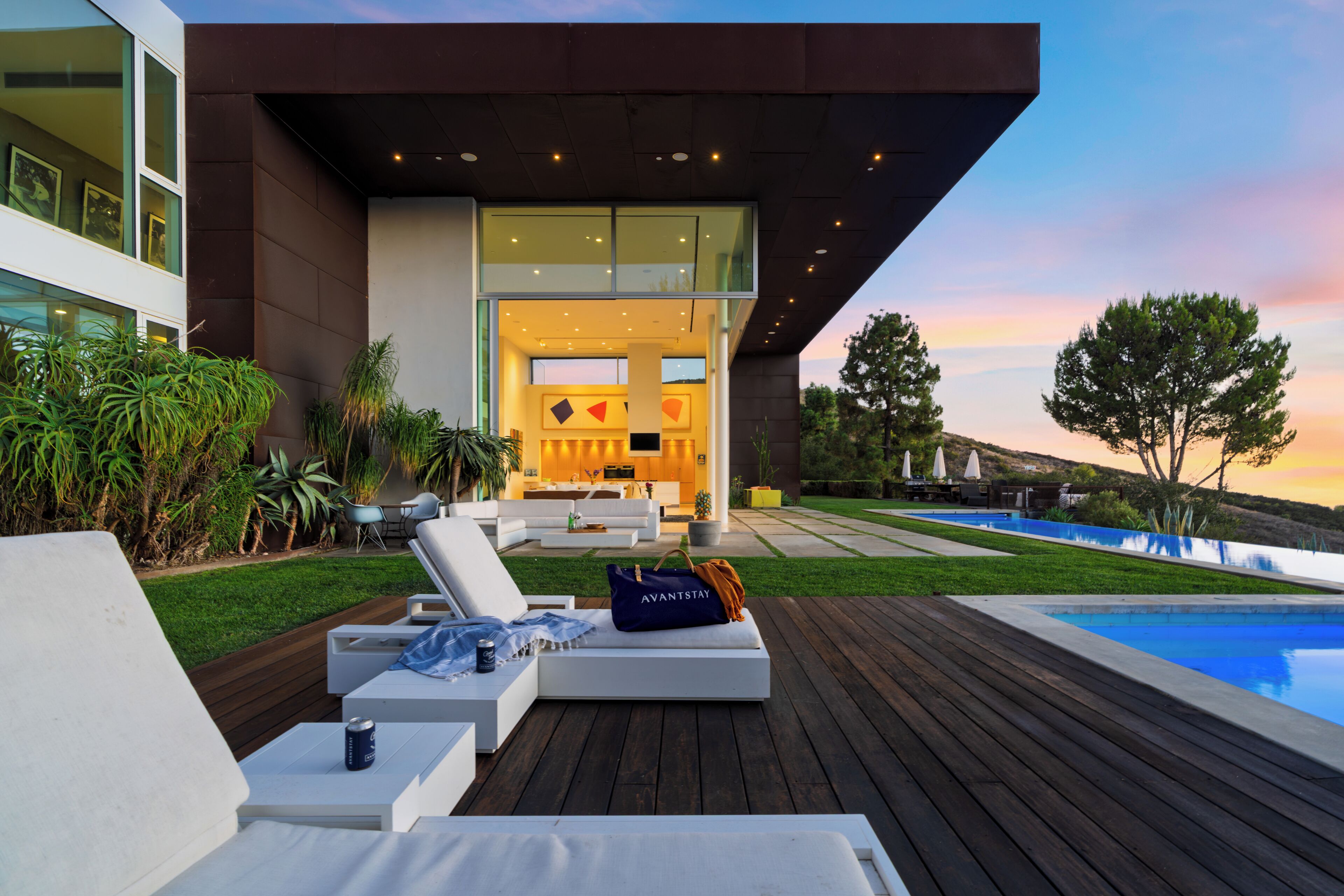 A modern outdoor lounge area with a pool, deck, and a view of the interior of a house.