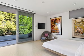 A modern bedroom with a large bed, a TV mounted on the wall, and a poster.