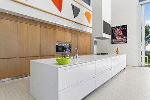 Een moderne keuken met een groot eiland, houten kastjes en een kleurrijk abstract schilderij.