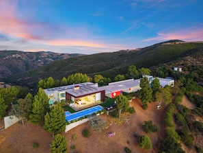 A modern house with a swimming pool, surrounded by trees and hills.