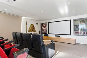 Un cine en casa moderno con sillones reclinables de cuero negro, un televisor de pantalla plana grande y carteles en la pared.