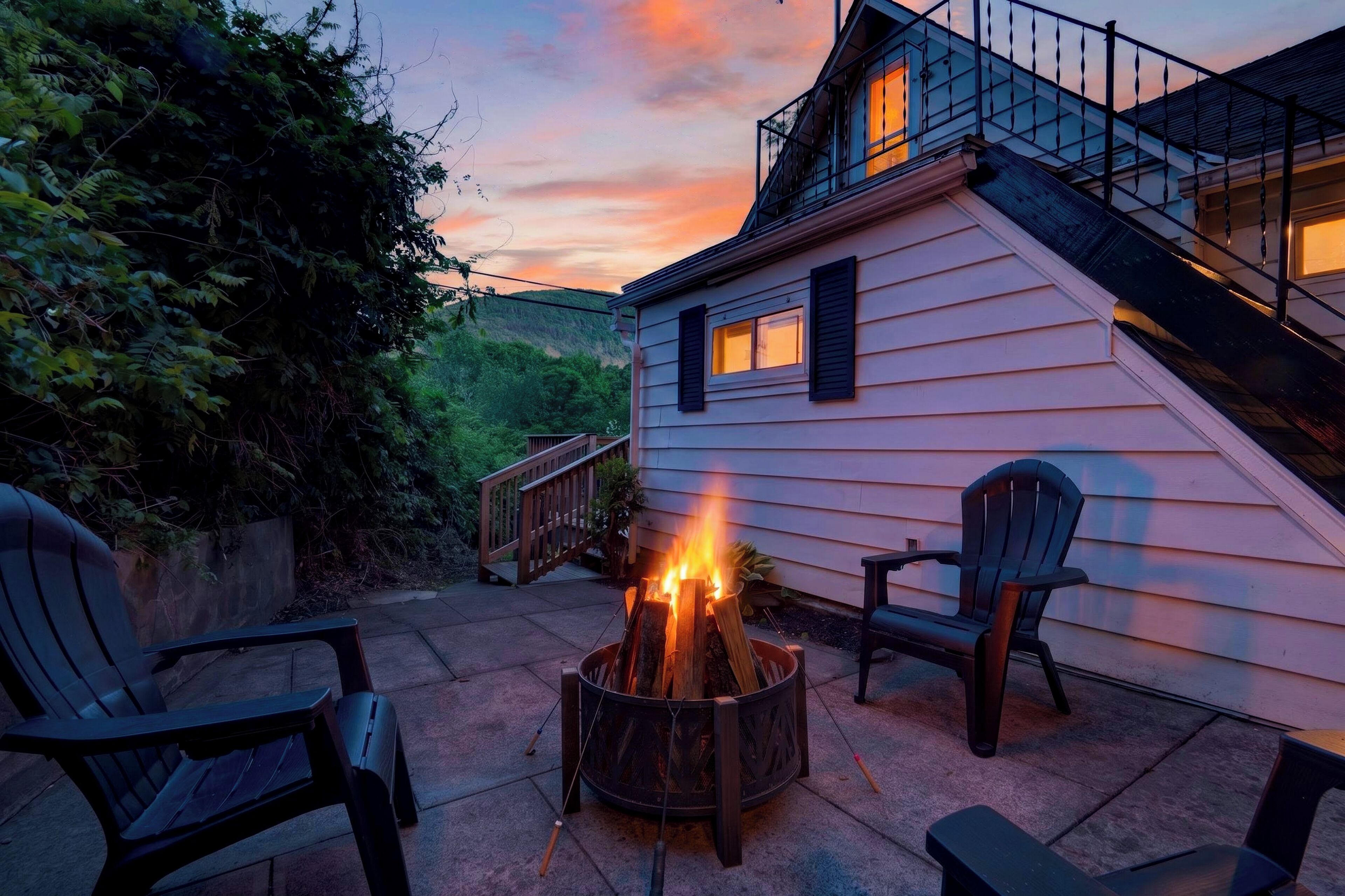 Ein Haus mit Feuerstelle im Garten, zwei Adirondack-Stühlen und einer Holzterrasse.
