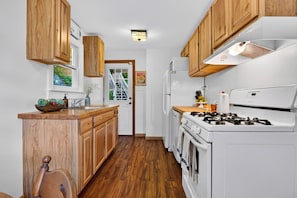 A kitchen with wooden cabinets, a white stove, and a refrigerator. - Firepit + Valley-View Deck | Creek + Valley Views + Slopes | Creekside Cabin (Lexington)