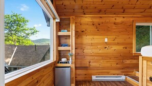 Uma cabana de madeira compacta com uma cozinha compacta, aquecedor embutido e janela com vista para a paisagem verde.
