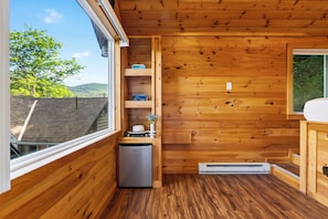 A compact wooden cabin with a small kitchenette, a built-in heater, and a window overlooking a green landscape. - Firepit + Valley-View Deck | Creek + Valley Views + Slopes | Creekside Cabin (Lexington)