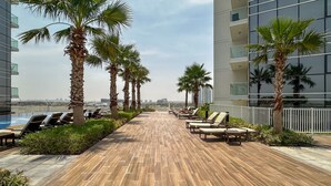 A rooftop lounge area with sun loungers, palm trees, and a view of the cityscape. - Elegant Studio Retreat in Damac Hills (Dubai)