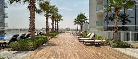 A rooftop lounge area with sun loungers, palm trees, and a view of the cityscape.