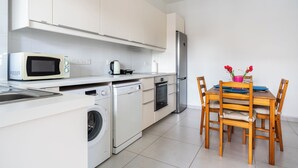 Eine moderne Küche mit Mikrowelle, Wasserkocher, Backofen und Waschmaschine. Es gibt einen Holztisch mit Stühlen und eine Vase mit roten Blumen.