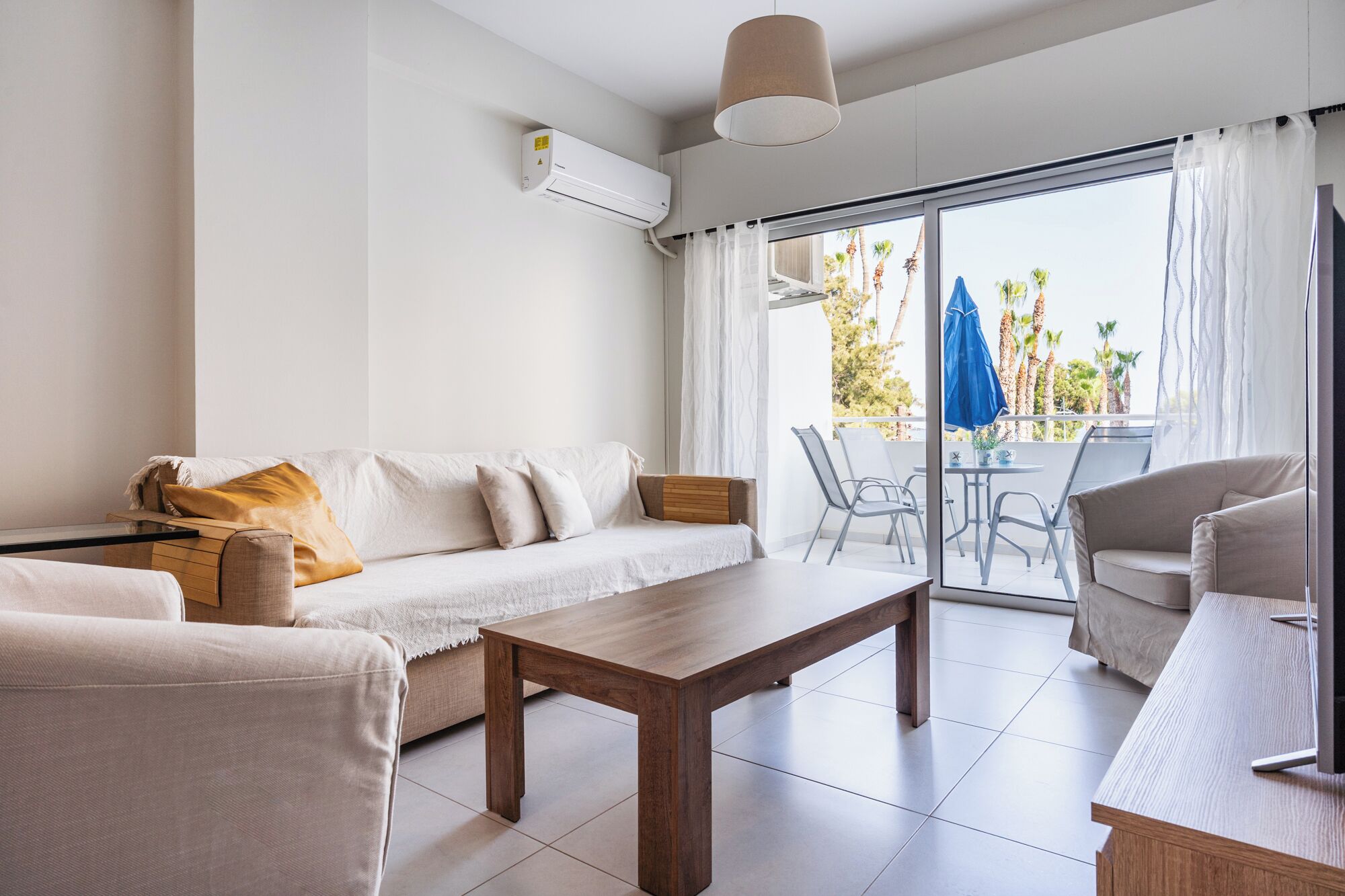Una sala de estar moderna con sofá, una mesa de centro de madera y un balcón con sillas y un paraguas azul.