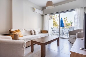 Un soggiorno moderno con un divano, un tavolino in legno e un balcone con sedie e un ombrellone blu.