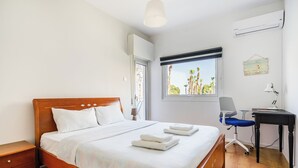 Ein Hotelzimmer mit einem Holzbett, einem Schreibtisch mit Stuhl und einem Fenster mit Blick auf Palmen.
