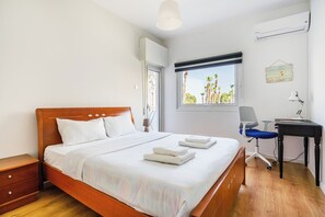 Una camera d'albergo con un letto in legno, una scrivania con una sedia e una finestra vista palme.