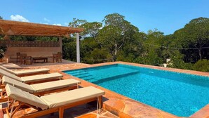 A rectangular swimming pool with clear blue water, surrounded by lounge chairs and a covered seating area.