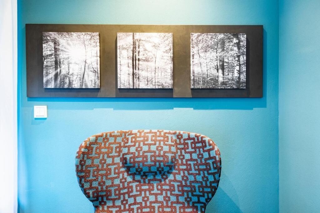 Quarto com parede azul, um quadro de uma floresta e uma escultura estampada.
