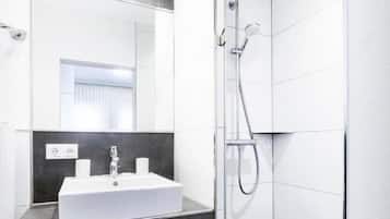 Un baño moderno con un lavamanos blanco, baldosas oscuras y una cabina de ducha de vidrio.