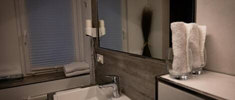 A bathroom with a white sink, a mirror, a towel rack, and a window with closed blinds.