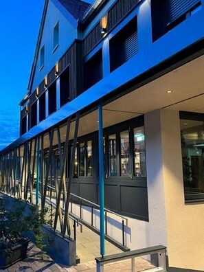 Un edificio moderno con fachada de vidrio, zona de estar al aire libre y una escalera que conduce a la entrada.