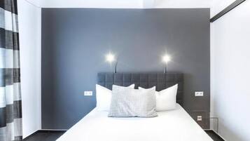 A modern hotel room with a large bed, two bedside lamps, and a dark wall.