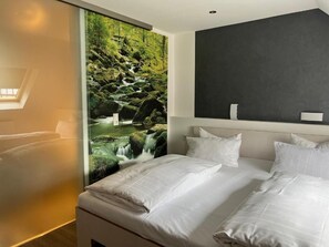 A hotel room with a bed, white bedding, a large window with a view of a waterfall, and a dark accent wall.