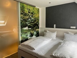 Habitación de hotel con cama, ropa de cama blanca, un ventanal con vistas a una cascada y una pared de acento oscura.