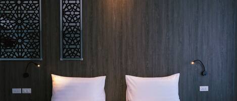 Habitación de hotel con pared de madera, dos camas con ropa blanca, un panel decorativo en la pared y dos lámparas fijadas a la pared.