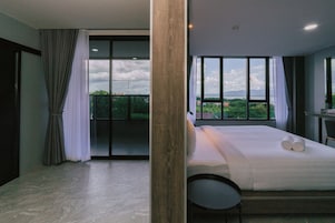 Un dormitorio moderno con una cama grande, una silla y vistas a un paisaje verde a través de amplios ventanales.