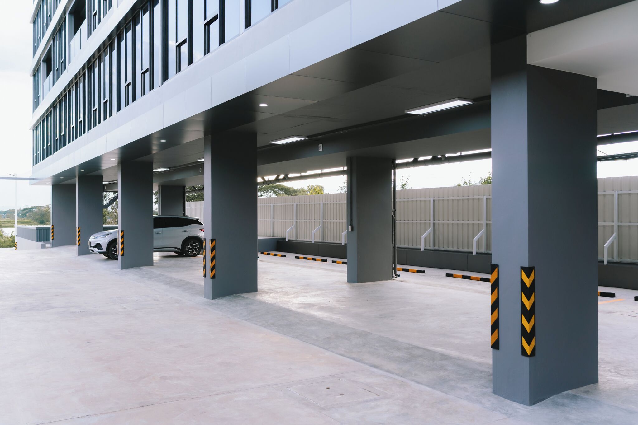Un edificio moderno con una zona de estacionamiento techada que muestra un automóvil blanco.
