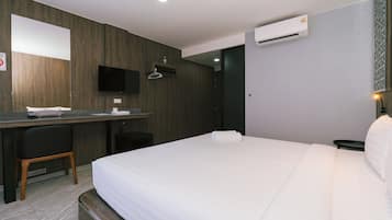 Una habitación de hotel con cama, escritorio, silla, televisión y aire acondicionado.