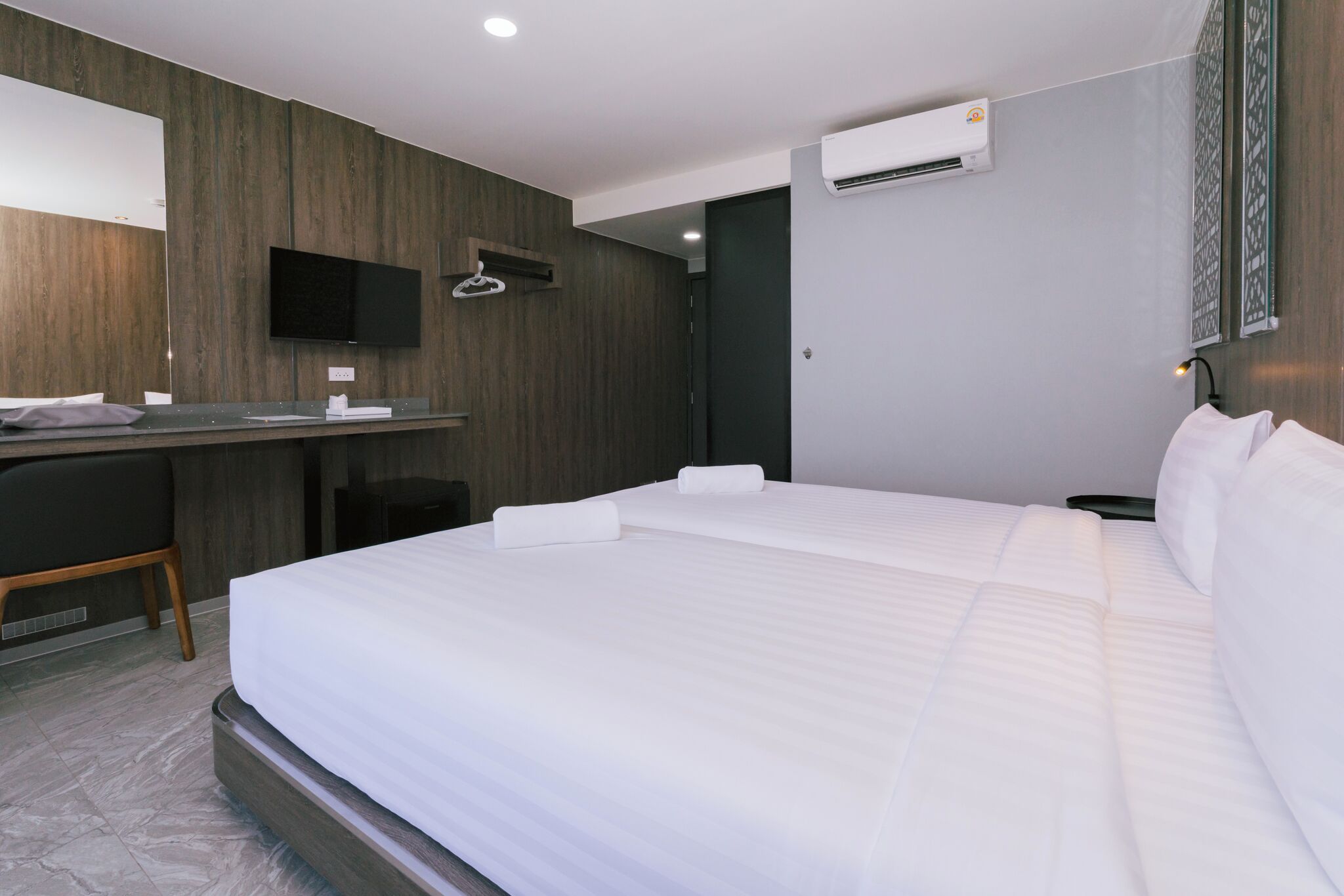 A hotel room with a bed, desk, chair, and an air conditioning unit.