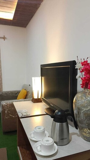 Una habitación con televisión de pantalla plana, cafetera y un florero con flores sobre una mesa.