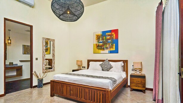 A hotel room with a wooden bed, two bedside tables, a wall-mounted artwork, a mirror, and a modern ceiling light fixture.