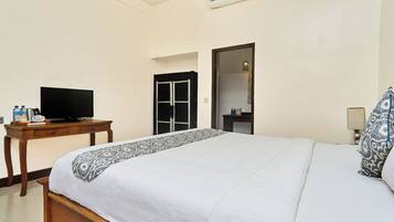 A hotel room with a bed, a television on a wooden table, a bathroom door, and a nightstand with a lamp.