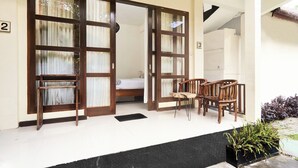 A room with a bed, a wooden chair, and a table. There are two doors with curtains.