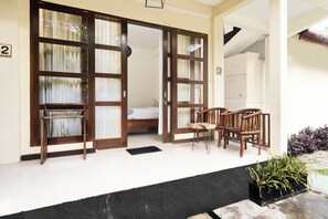A room with a bed, a wooden chair, and a table. There are two doors with curtains.