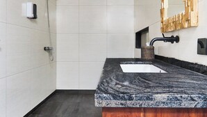 A modern bathroom with a marble countertop, a wooden vanity, a large mirror, and a shower.