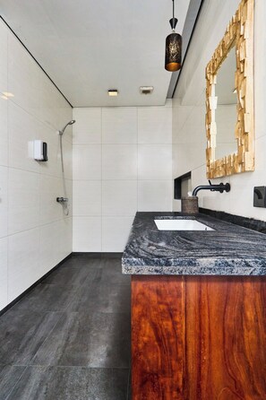 A modern bathroom with a marble countertop, a wooden vanity, a large mirror, and a shower.
