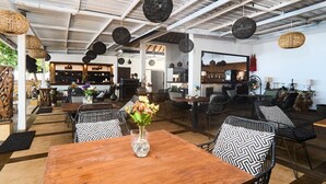 An indoor dining area with wooden tables and black and white patterned chairs, a central vase with flowers, and hanging spherical light fixtures.