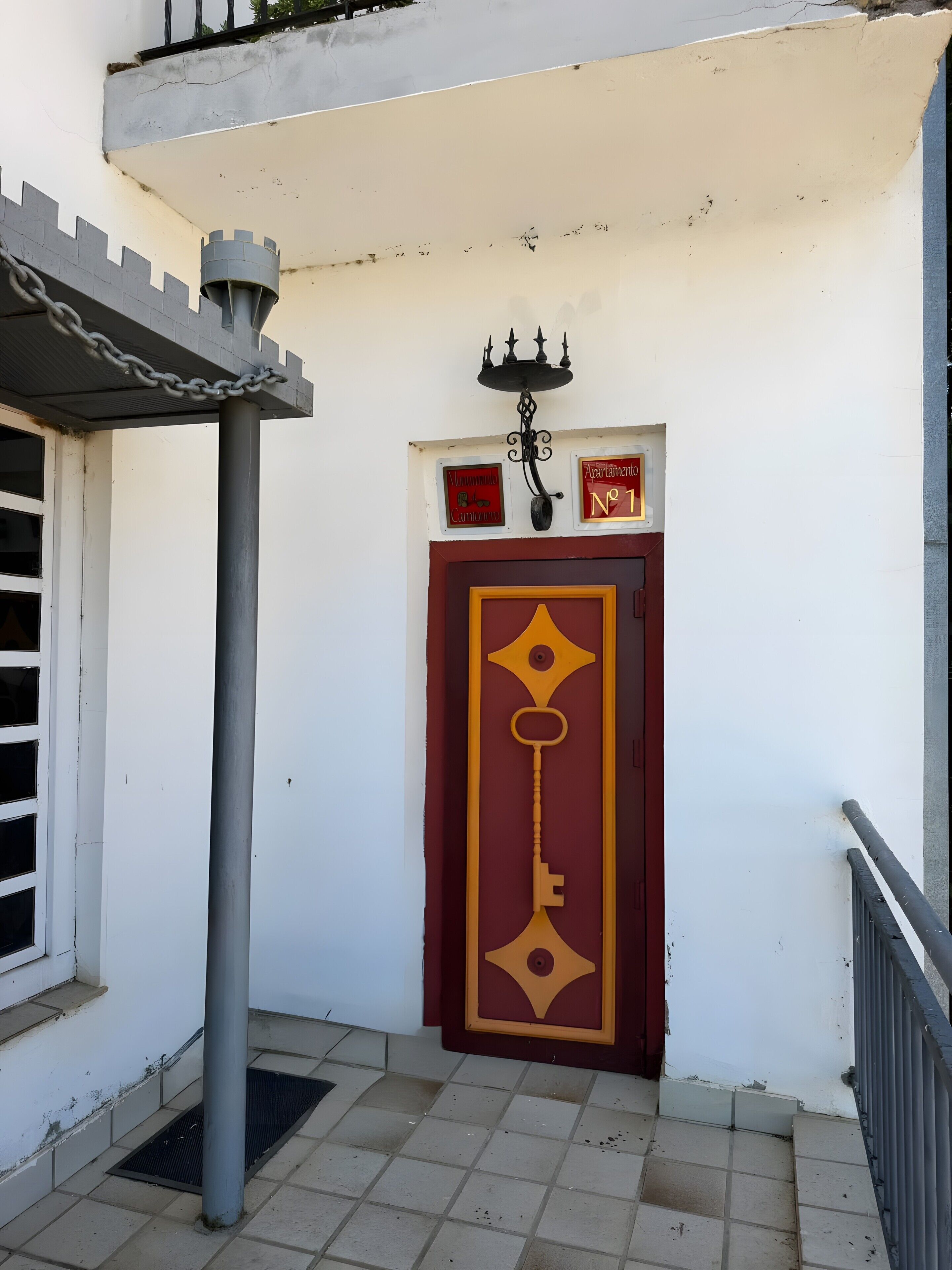 Entrada de un edificio con puerta roja, portón metálico y un cartel en la pared.