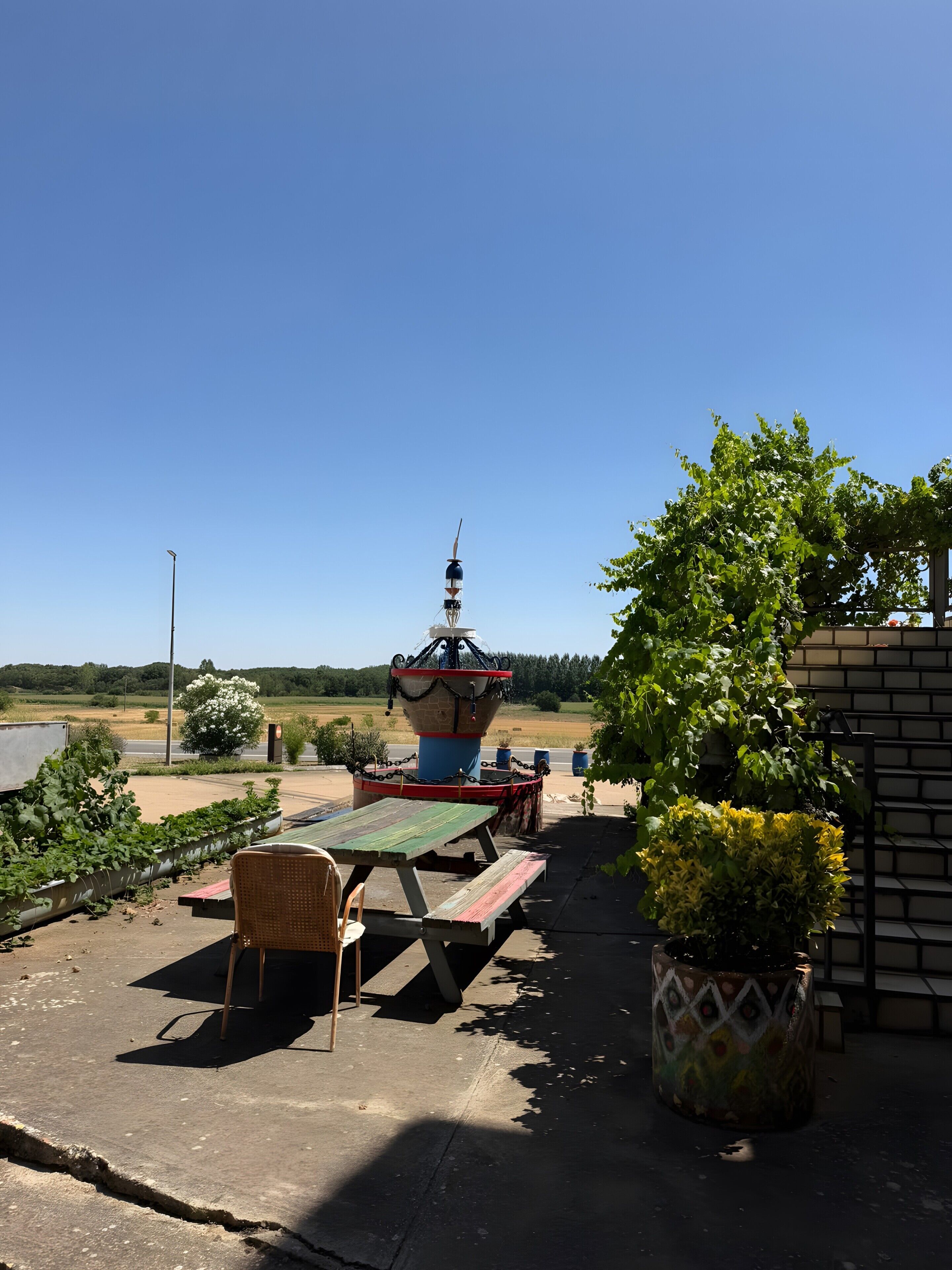 Un espacio al aire libre con mesa y sillas, una fuente decorativa y vistas del paisaje.